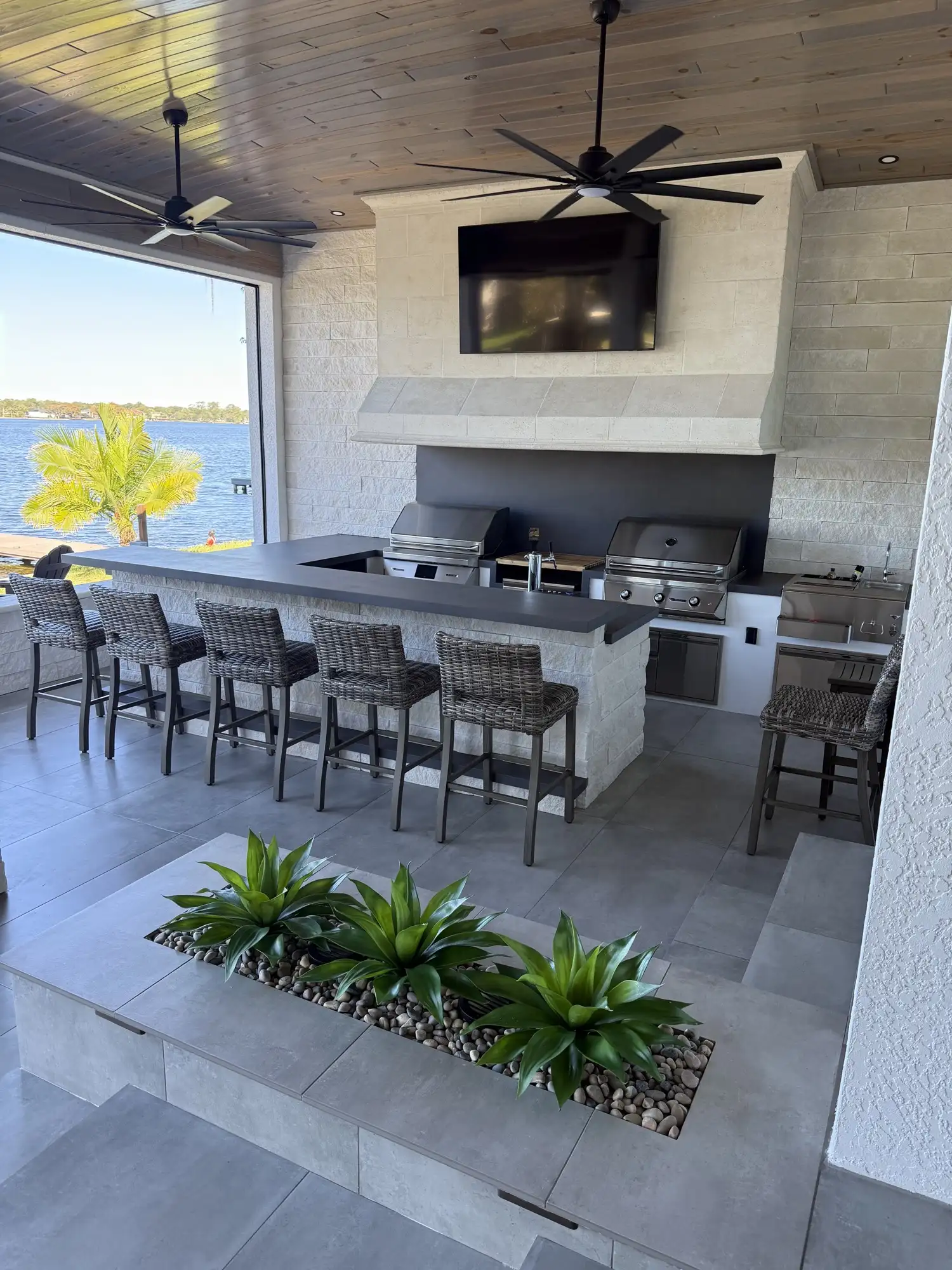 The covered lanai with mounted TV, bar seating, and lit planter wall in the evening